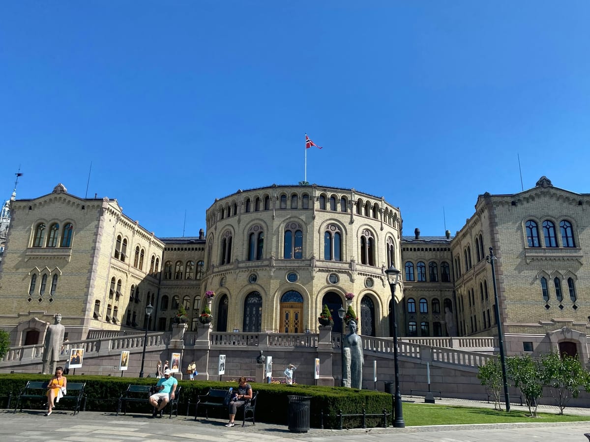 Stortingsbygningen i Oslo en solskinnsdag med norsk flagg på taket